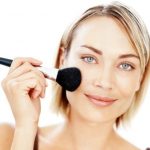 Portrait of an attractive young woman applying blusher on white background